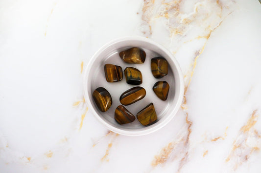 Tumbled tigers eye stones from Solstice et Mineraux in a white bowl on marble surface