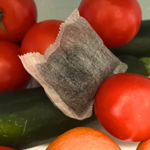 BIJIN black charcoal water filter entire house bag with white mesh material surrounded by fresh red tomatoes and green cucumber