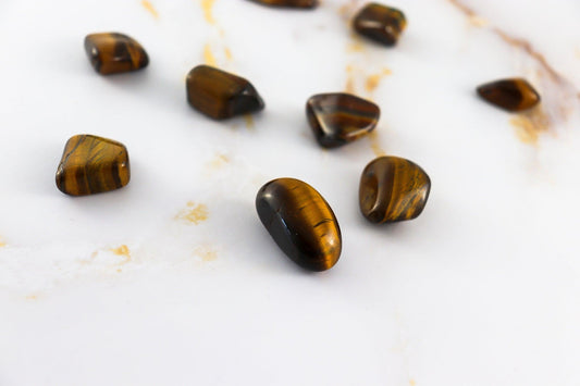 Polished tigers eye pierre roulée stones by Solstice et Mineraux displayed on a white marble surface