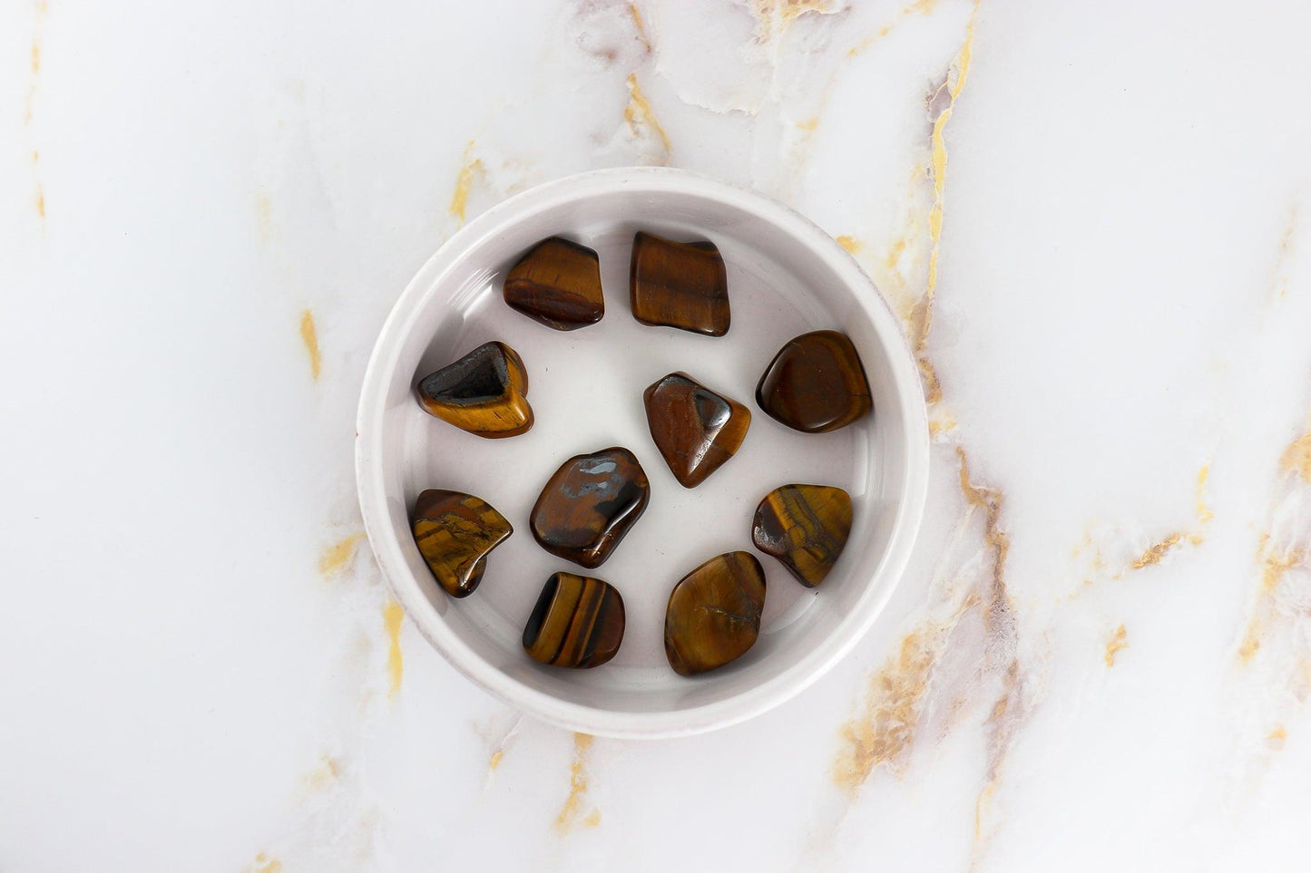 Solstice et Mineraux tigers eye pierre roulée stones polished and displayed in a white bowl on marble surface