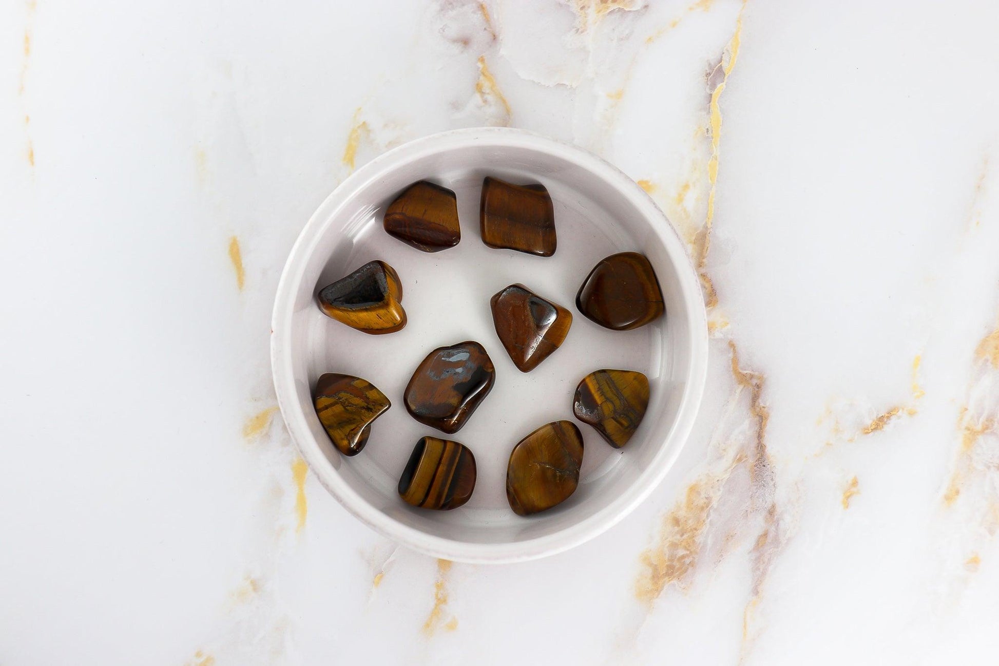 Solstice et Mineraux tigers eye pierre roulée stones polished and displayed in a white bowl on marble surface