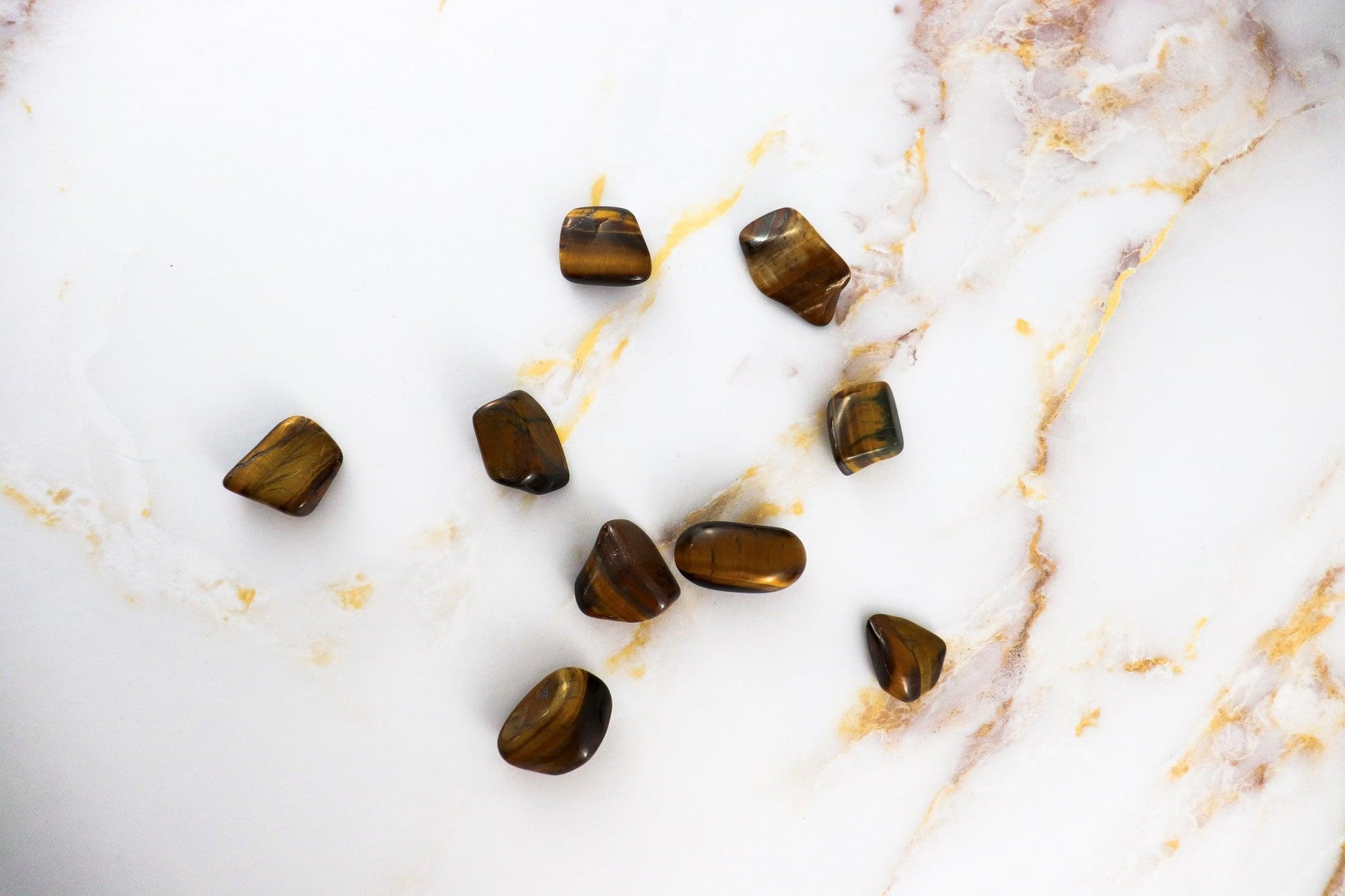 Solstice et Mineraux polished pierre roulée tigers eye stones on white marble background